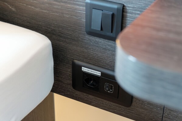 A bathroom with a dark wood-textured wall, a white sink, and a black electrical outlet with a label. - easyHotel Zurich City Main Station  (Zürich)