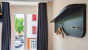A room with a large window, black curtains, a radiator, and a wall-mounted shelf with a coat rack.