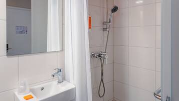Un bagno con lavandino bianco, uno specchio, una doccia con soffione a mano e una porta doccia in vetro.