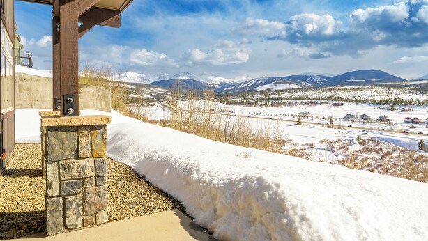 Paisaje nevado con montañas al fondo, una estructura de piedra y una pérgola de madera.