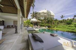Un espace aménagé au bord de la piscine, avec des chaises longues, des parasols et une vue sur un jardin luxuriant.