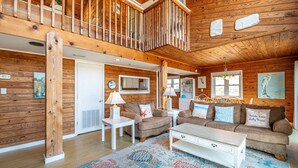 A spacious living area with a wooden interior, a white sofa set, a coffee table, and a colorful rug. - Cavallo Dunes - 4x4 Carova Beach, Oceanfront, Ocean View, Hot Tub, Pets OK, Year Round Flex Stays (4x4 - Carova Beach)