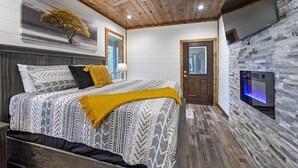 A bedroom with a bed, a ceiling fan, a wall-mounted TV, and a stone wall. - 3 bedroom with game room! (Broken Bow)
