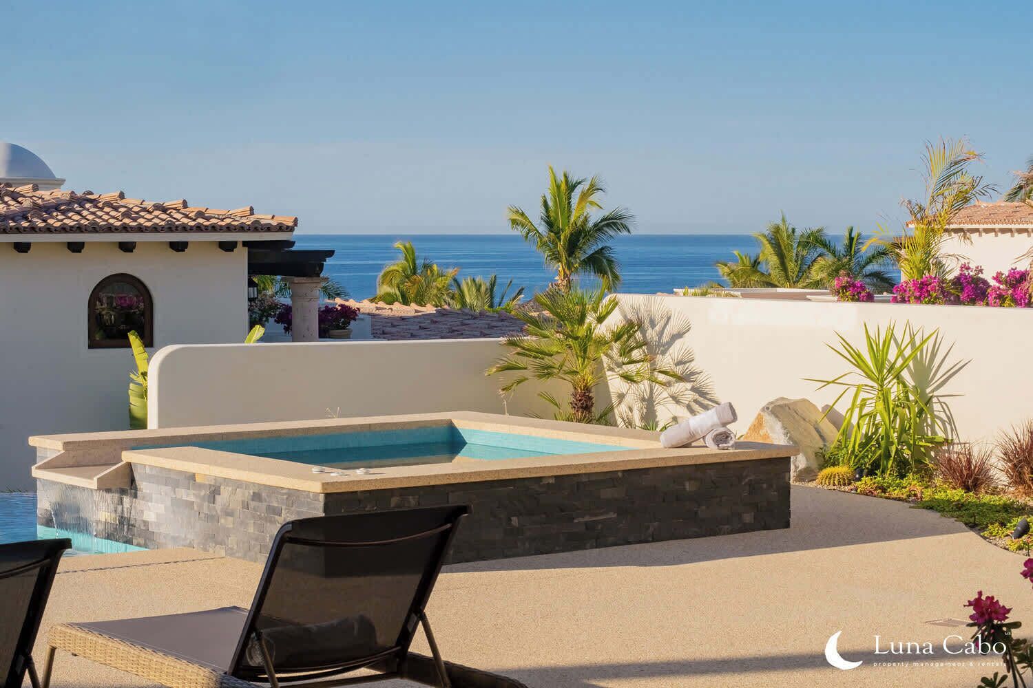 A pool area with a hot tub, lounge chairs, and a view of the ocean.
