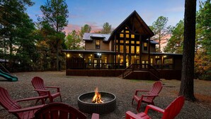 Un chalet doté d’un foyer extérieur et de chaises Adirondack rouges dans la cour.