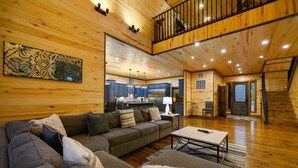 Un vaste espace de vie avec un intérieur en bois, un ensemble de canapés, une table basse et une cuisine en arrière-plan.