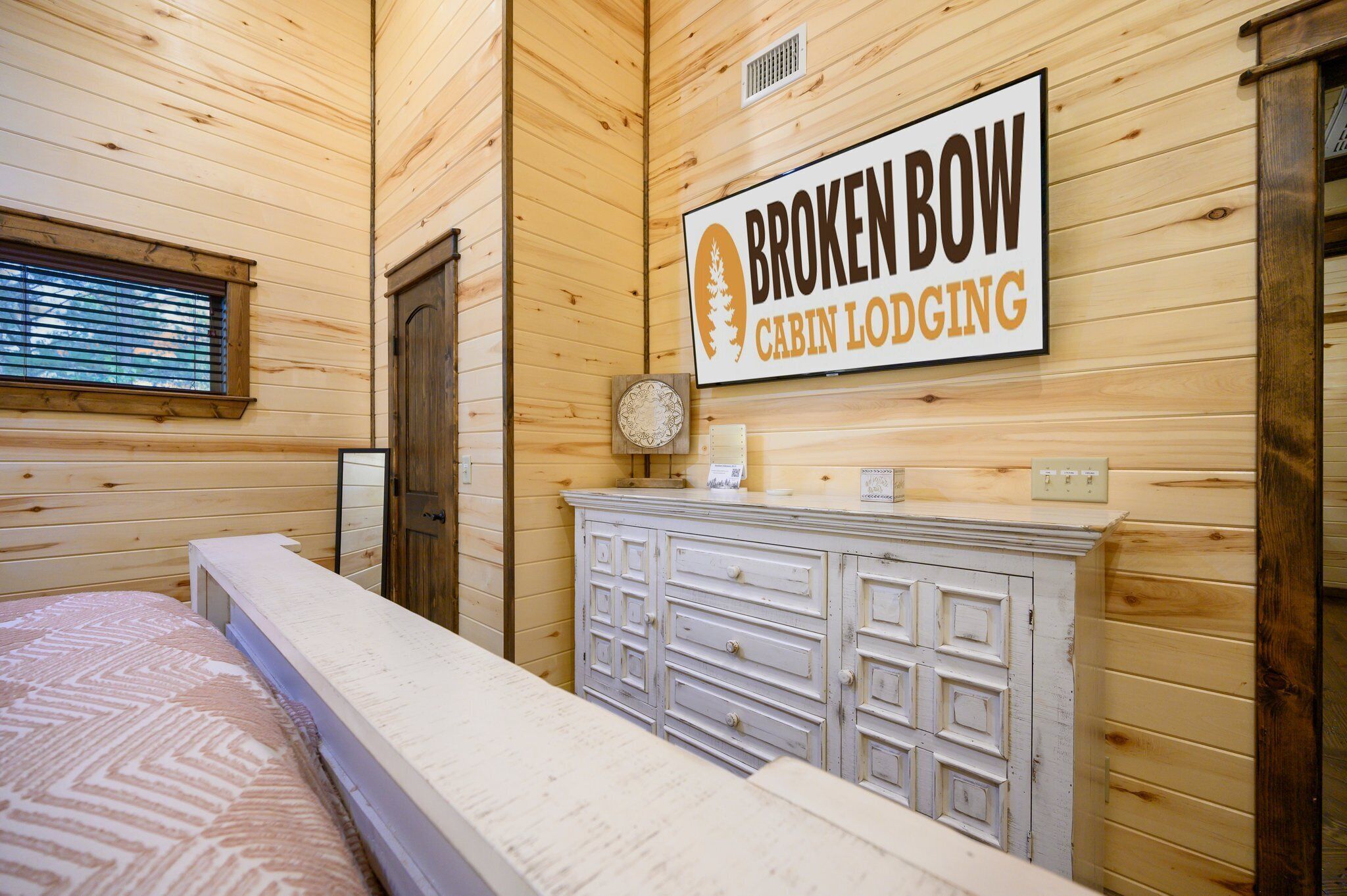 Une cabane équipée d’un lit, d’une commode et d’une pancarte indiquant « CABANES DE BROKEN BOW – HÉBERGEMENT ».