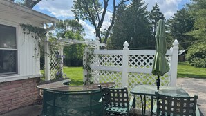 A patio with a table and chairs, a white fence, and trees in the background. - Large House Rental in Historic Area (Indianapolis)
