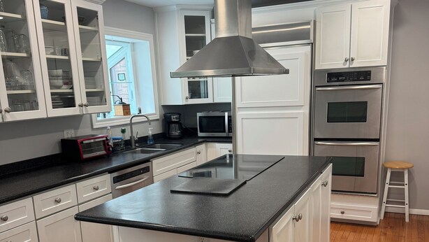 A modern kitchen with white cabinetry, a central island, stainless steel appliances, and wooden flooring. - Large House Rental in Historic Area (Indianapolis)