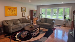 A living room with two sofas, a coffee table, a cabinet, and a window with a view of greenery. - Large House Rental in Historic Area (Indianapolis)