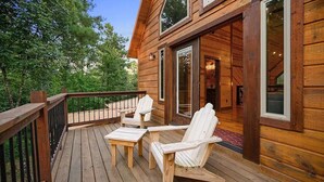 Een houten terras met Adirondack-stoelen en een glazen deur naar een binnenruimte.
