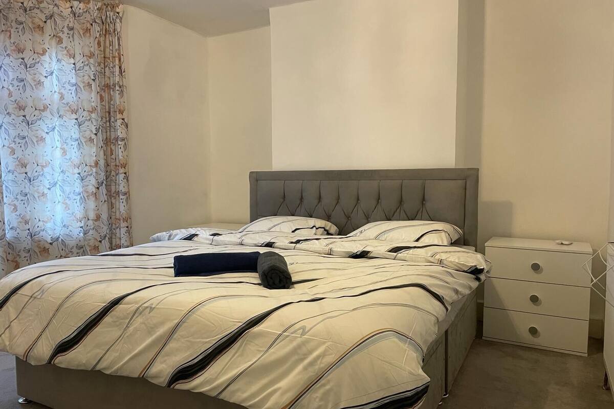 Una cama bien hecha con una colcha a rayas, un cabecero tapizado gris y una mesita de noche con cajones.