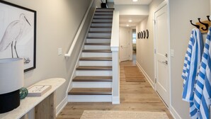 Eine Treppe, die zu einer zweiten Etage führt, ein gerahmtes Vogelbild an der Wand, ein Handtuchhalter mit Handtüchern und ein Holzboden.