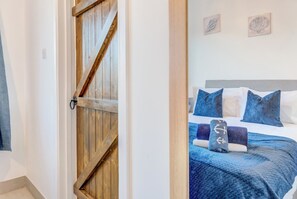 A bedroom with a wooden door, a bed with blue bedding, and two wall-mounted artworks. - Sun Valley Hideaway (Saundersfoot)