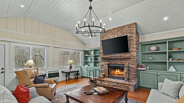 A spacious living room with a stone fireplace, comfortable seating, and a television mounted above it. - Duck's Nest 3BR: Modern Creekside Retreat w/ Large Deck, Private Lower Suite (Highlands)