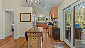 A spacious kitchen with wooden cabinets, a central island, and a large window offering a view of the outdoors. - Duck's Nest 3BR: Modern Creekside Retreat w/ Large Deck, Private Lower Suite (Highlands)