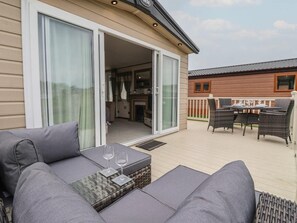 A modern outdoor living area with a sofa, a glass-top table, and a dining set. - Whispering Willows 2-bed Lodge in Scarborough (Scarborough)