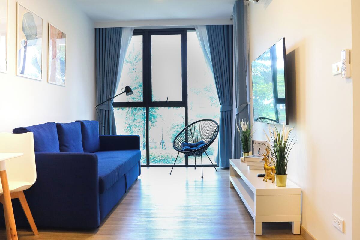 A modern living room with a blue sofa, a black chair, a white console table, and a large window with curtains.