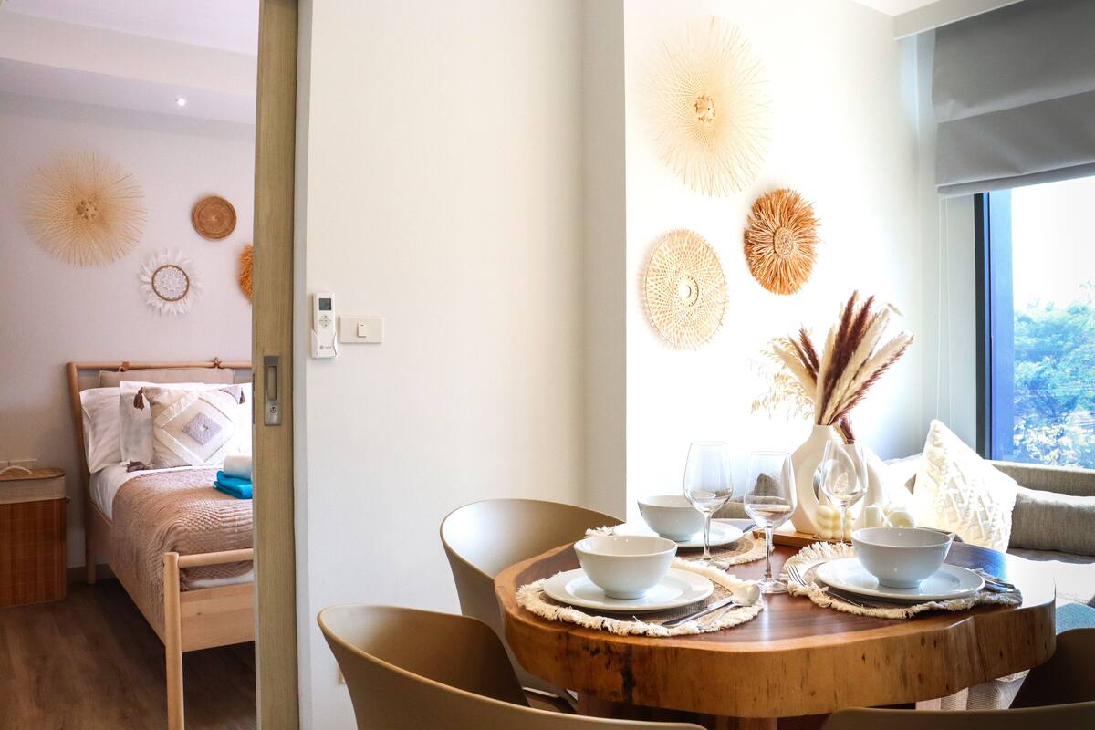 A modern room with a wooden bed, a dining table with white bowls and wine glasses, and decorative wall art.