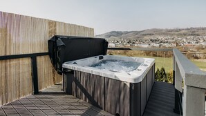 A hot tub on a wooden deck with a view of a town in the background. - Platz, Charme & ein Hauch Luxus: Happy Place mit Whirlpool, Sauna und Traumblick (Plettenberg)