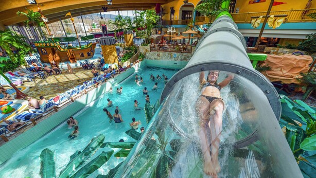 A water slide with a person at the top, a pool area with people, and a ship-themed structure. - Platz, Charme & ein Hauch Luxus: Happy Place mit Whirlpool, Sauna und Traumblick (Plettenberg)