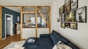 A modern living room with a dark blue sofa, wooden beams, and framed wildlife photographs on the wall. - Platz, Charme & ein Hauch Luxus: Happy Place mit Whirlpool, Sauna und Traumblick (Plettenberg)