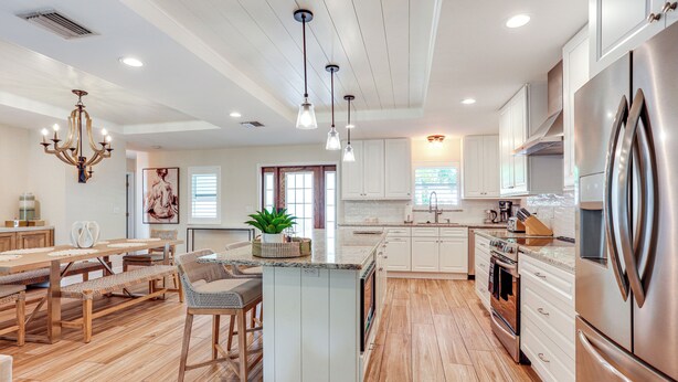 A spacious kitchen with wooden flooring, white cabinetry, a large island, stainless steel appliances, and pendant lighting. - Fenced Yard, 4 Mi to Stuart Beach: Family Retreat! (Stuart)