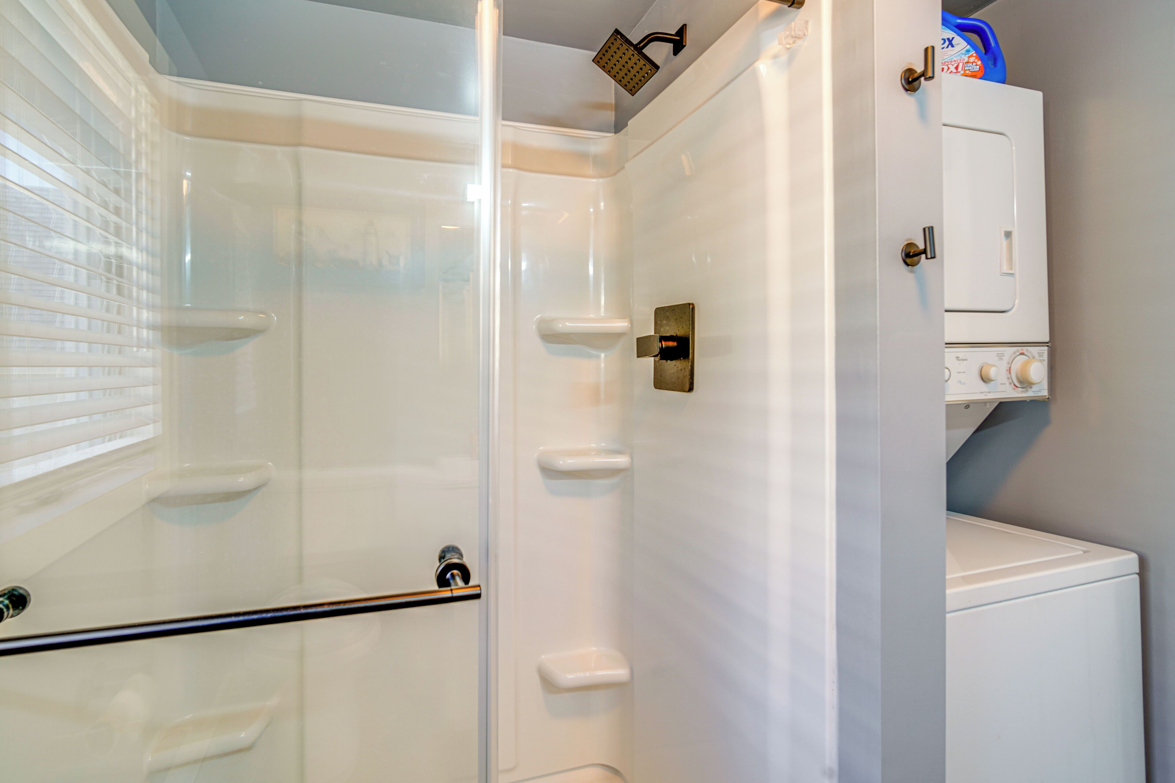 A bathroom with a glass-enclosed shower, a white toilet, and a white cabinet with a blue detergent bottle on top.