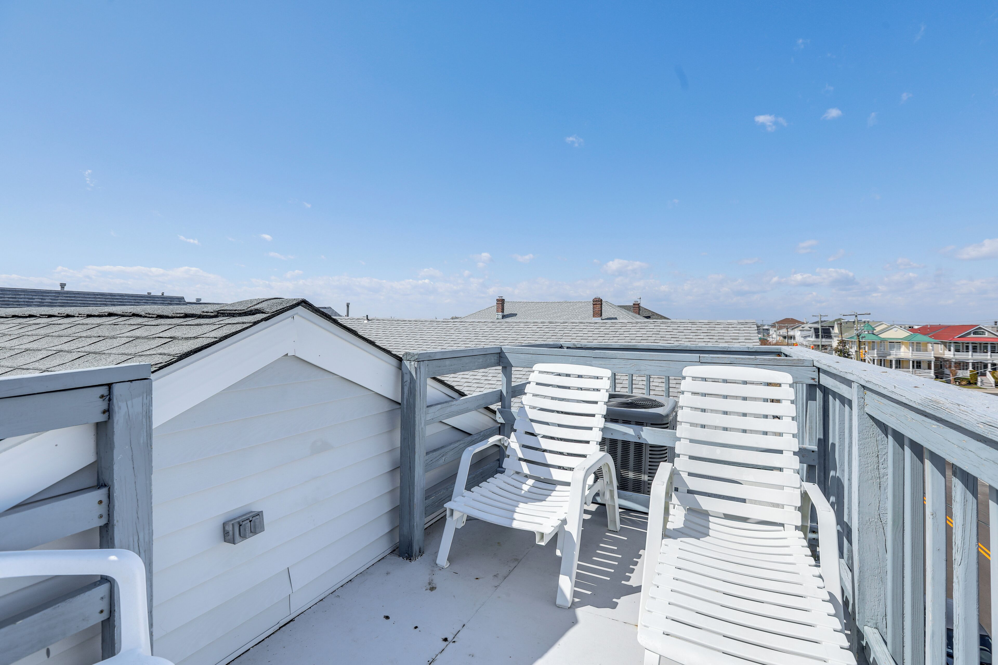 A rooftop deck with white chairs and a table, overlooking a residential area.