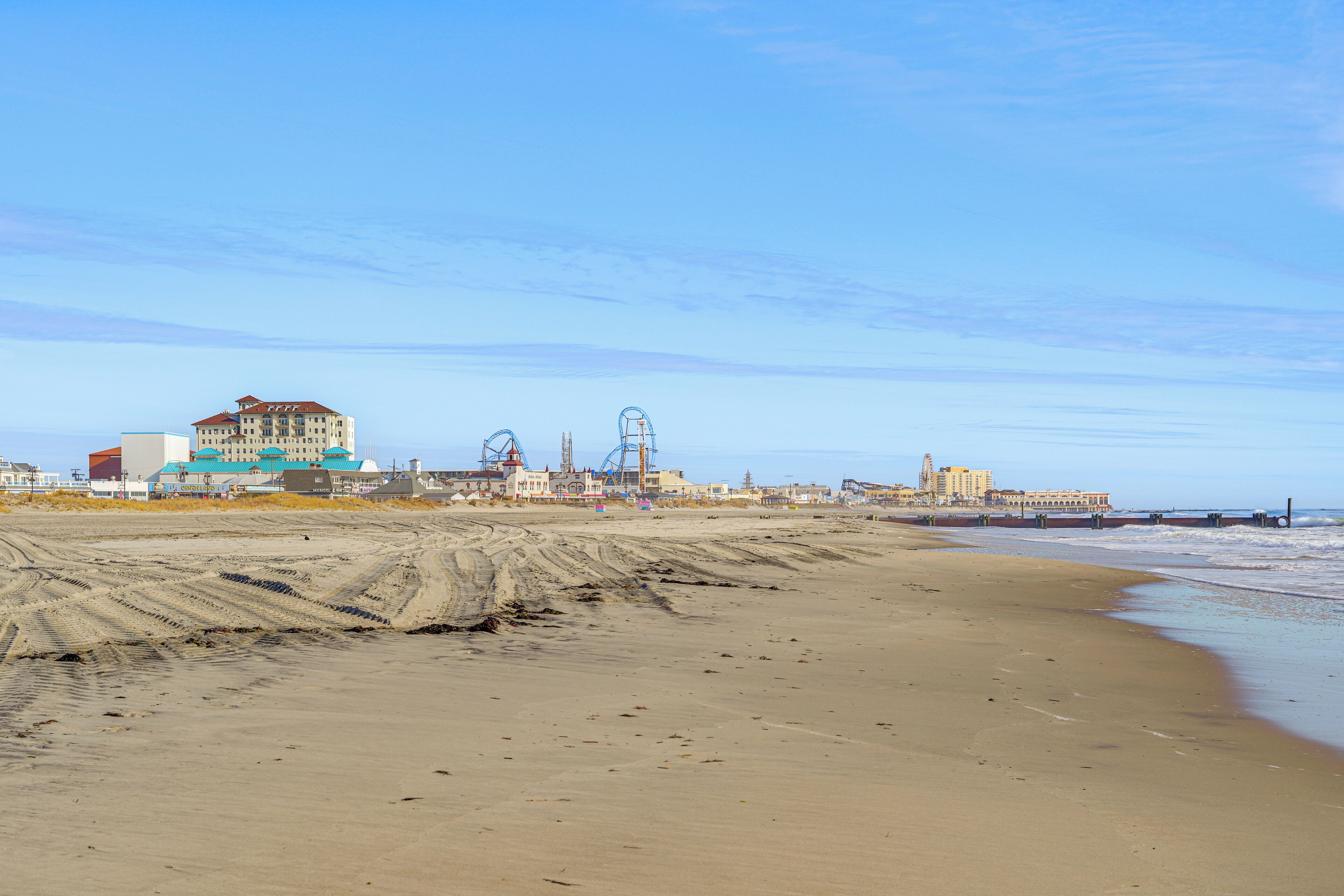 Una playa con un edificio grande y una montaña rusa al fondo.