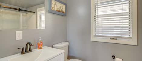 Een badkamer met een wit wastafelmeubel, een toilet en een raam met zonwering.