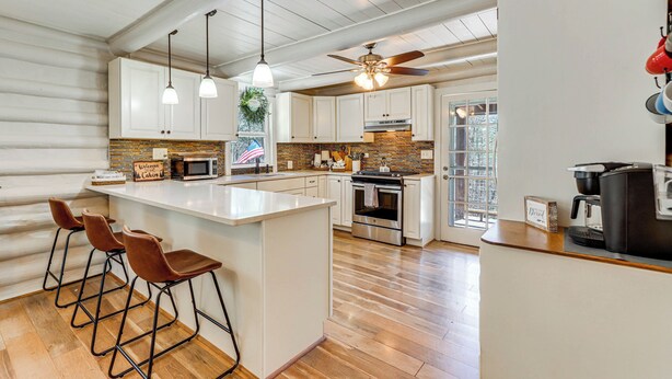 A kitchen with white cabinets, a central island with bar stools, a ceiling fan, and a coffee machine. - Dog-friendly Hiawassee Cabin Near Lake & Hiking (Hiawassee)