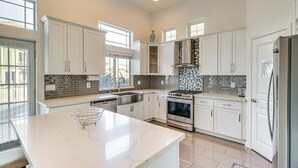 Una cocina moderna con armarios blancos, una isla grande, una estufa de acero inoxidable y un salpicadero de azulejos.