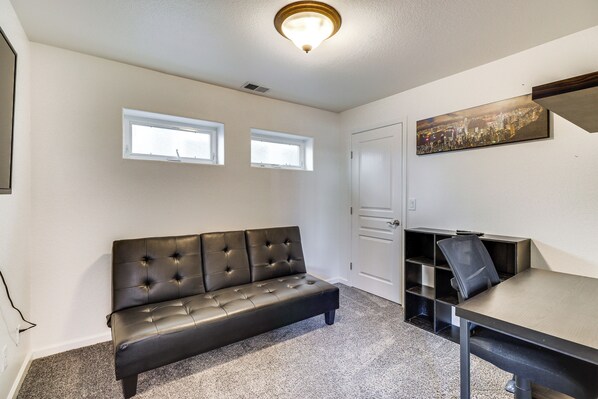 A room with a black leather sofa, a desk with a chair, two windows, and a cityscape painting on the wall. - Theater Room, Fireplace: Home 5 Mi to Dtwn Reno! (Sparks)