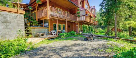 A wooden cabin with a balcony, surrounded by greenery and a gravel path.