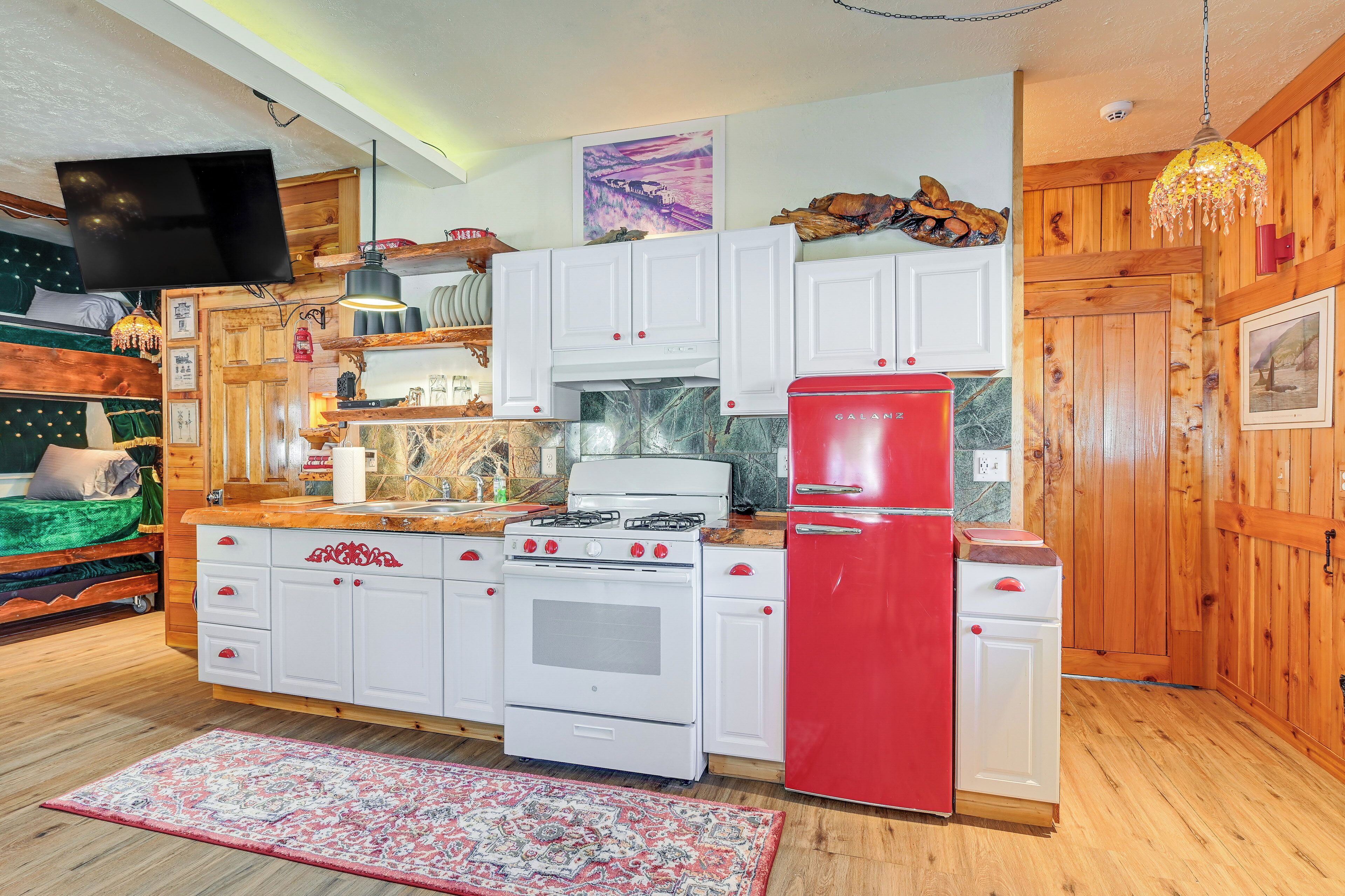 A compact kitchen with white cabinets, a red refrigerator, and a gas stove.