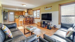 A spacious living area with a large TV, wooden furniture, and a view of the water. - Delton Lake House w/ Boat Dock: Fish, Swim & More! (Delton)