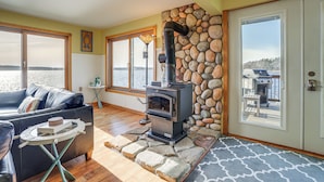 A cozy living room with a stone fireplace, a sofa, and a view of the water outside. - Delton Lake House w/ Boat Dock: Fish, Swim & More! (Delton)