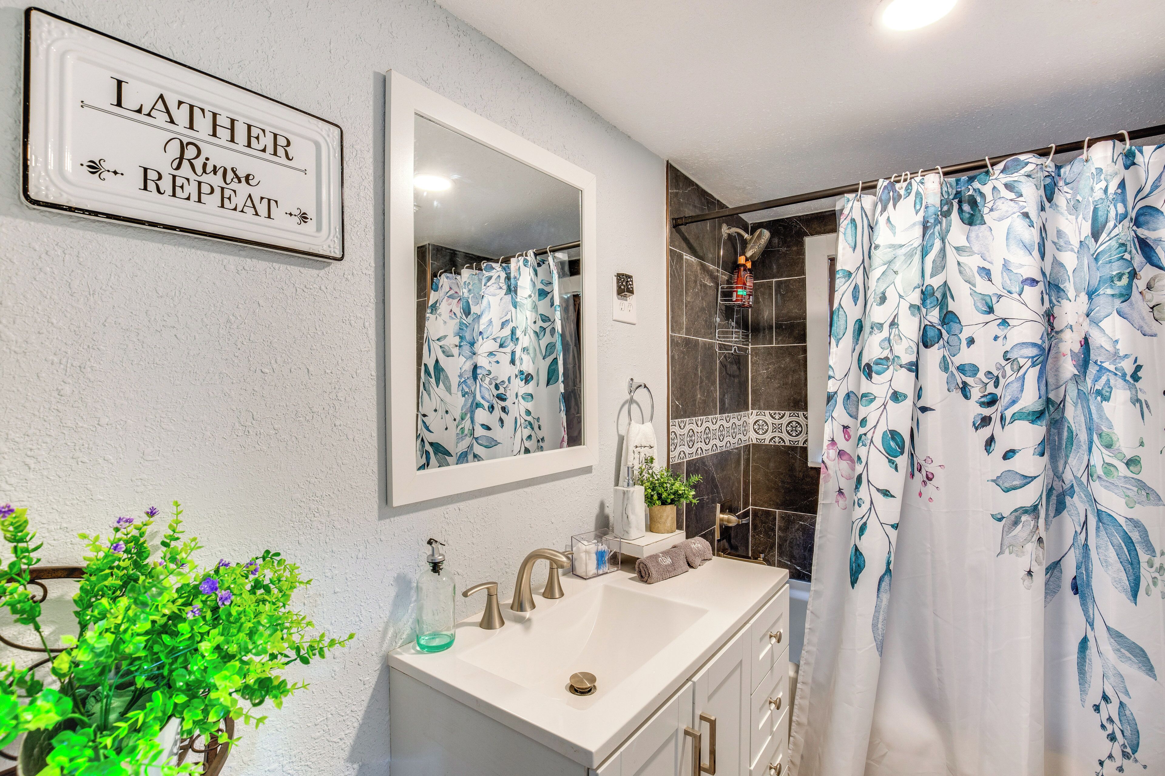 A bathroom with a sink, mirror, shower, and a sign that reads "LATHER Rinse Repeat".
