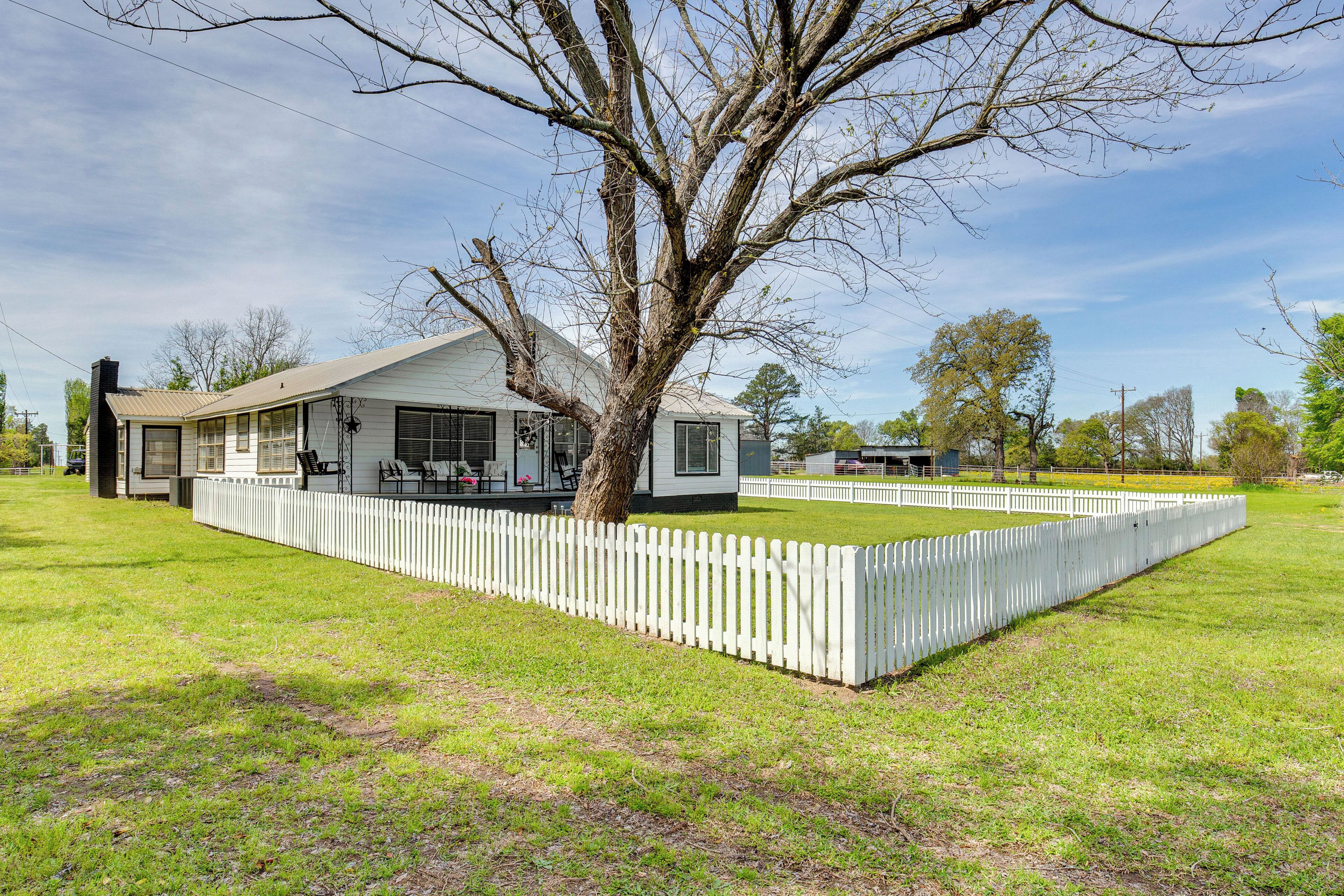 A single-story house with a white exterior, a large tree in front, and a white picket fence.