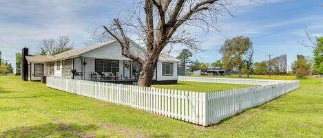 A single-story house with a white exterior, a large tree in front, and a white picket fence.