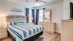 Um quarto com cama, mesas de cabeceira, cômoda, espelho e ventilador de teto.