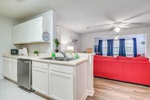 A modern kitchen with white cabinetry, a dishwasher, and a red sofa in the living area.