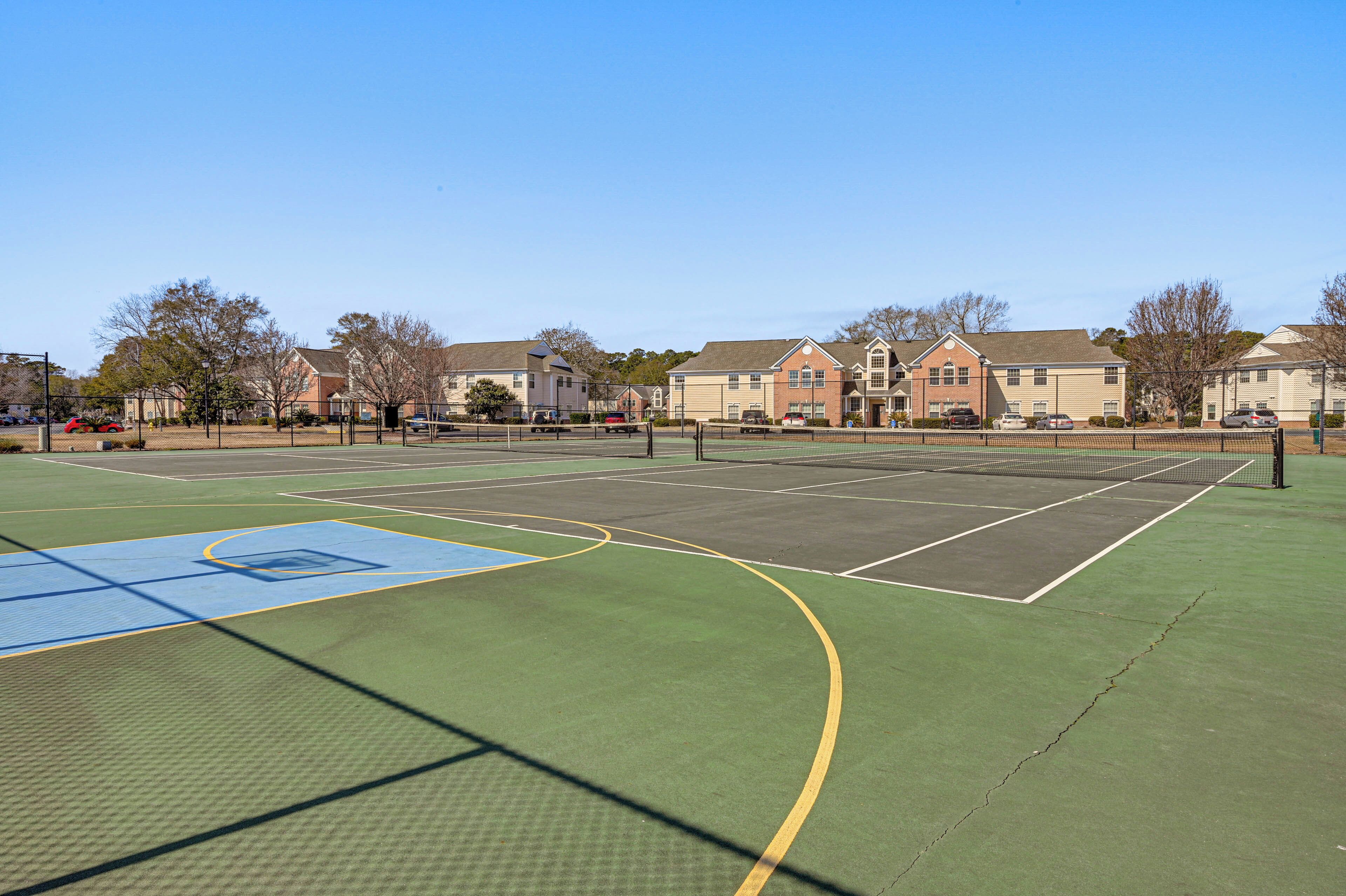 Un court de tennis en plein air, doté d’un filet, entouré d’immeubles d’habitation.