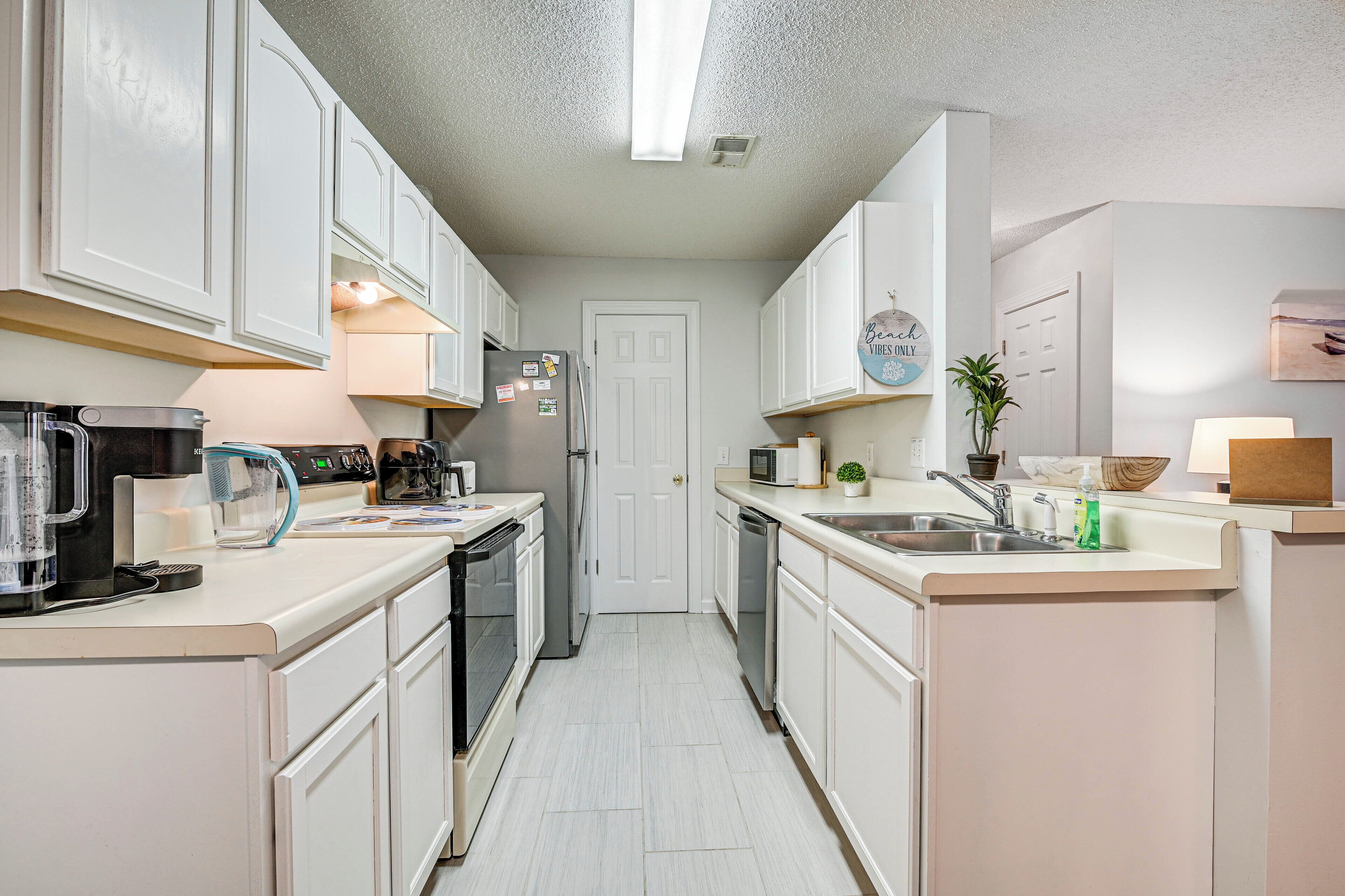 A kitchen with white cabinets, a refrigerator, a microwave, a coffee maker, and a sink.