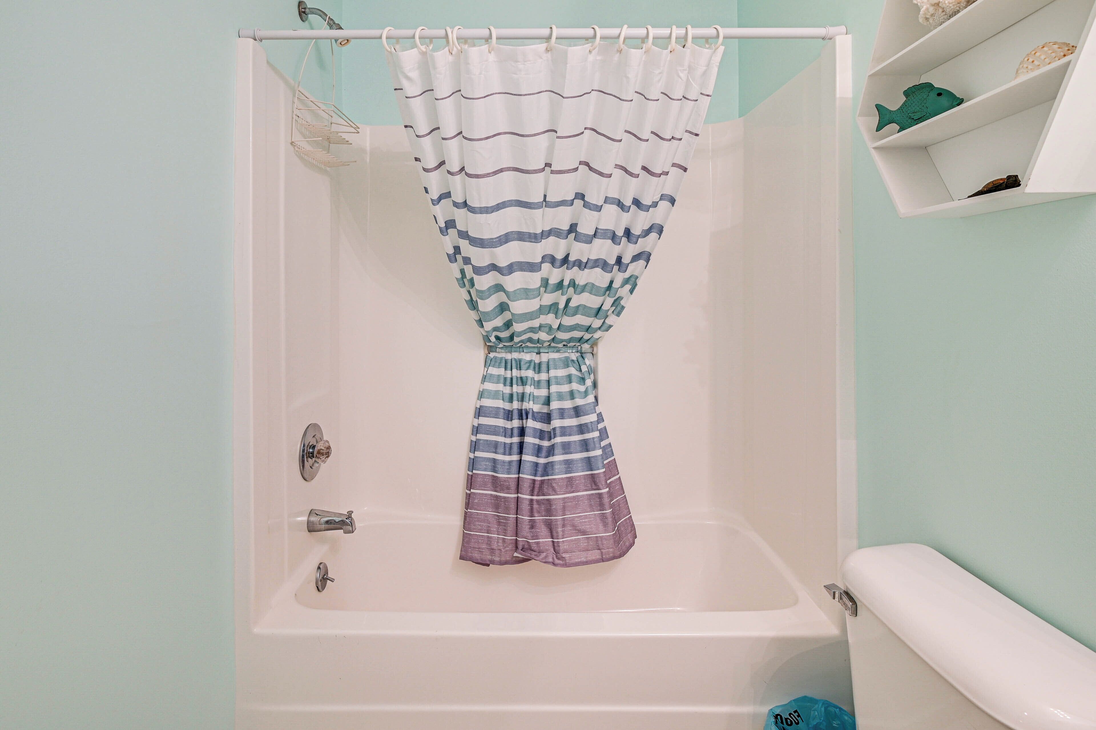 A bathtub with a striped shower curtain, a white shelf with decorative items, and a white bathtub with a faucet.