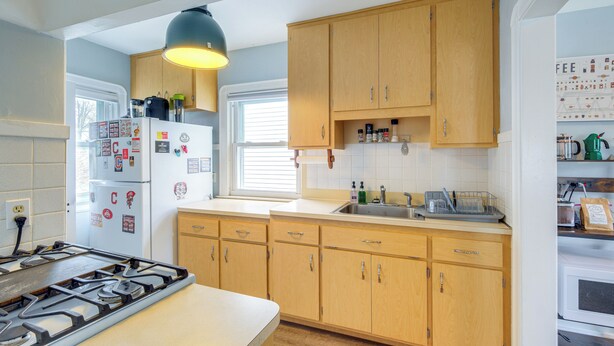 A kitchen with wooden cabinets, a gas stove, a refrigerator, and a window with blinds. - Wfh-friendly Abode w/ Home Gym in Cleveland (Cleveland)