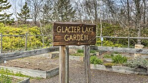 Ein Holzschild mit der Aufschrift 'Glacier Lake Garden', im Hintergrund ein Zaun und Blumenbeete.