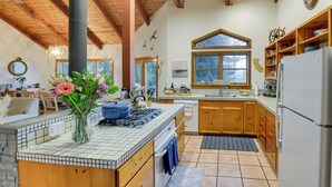 Une cuisine avec des meubles en bois, un grand îlot central doté d’une cuisinière et une fenêtre donnant sur un paysage enneigé.