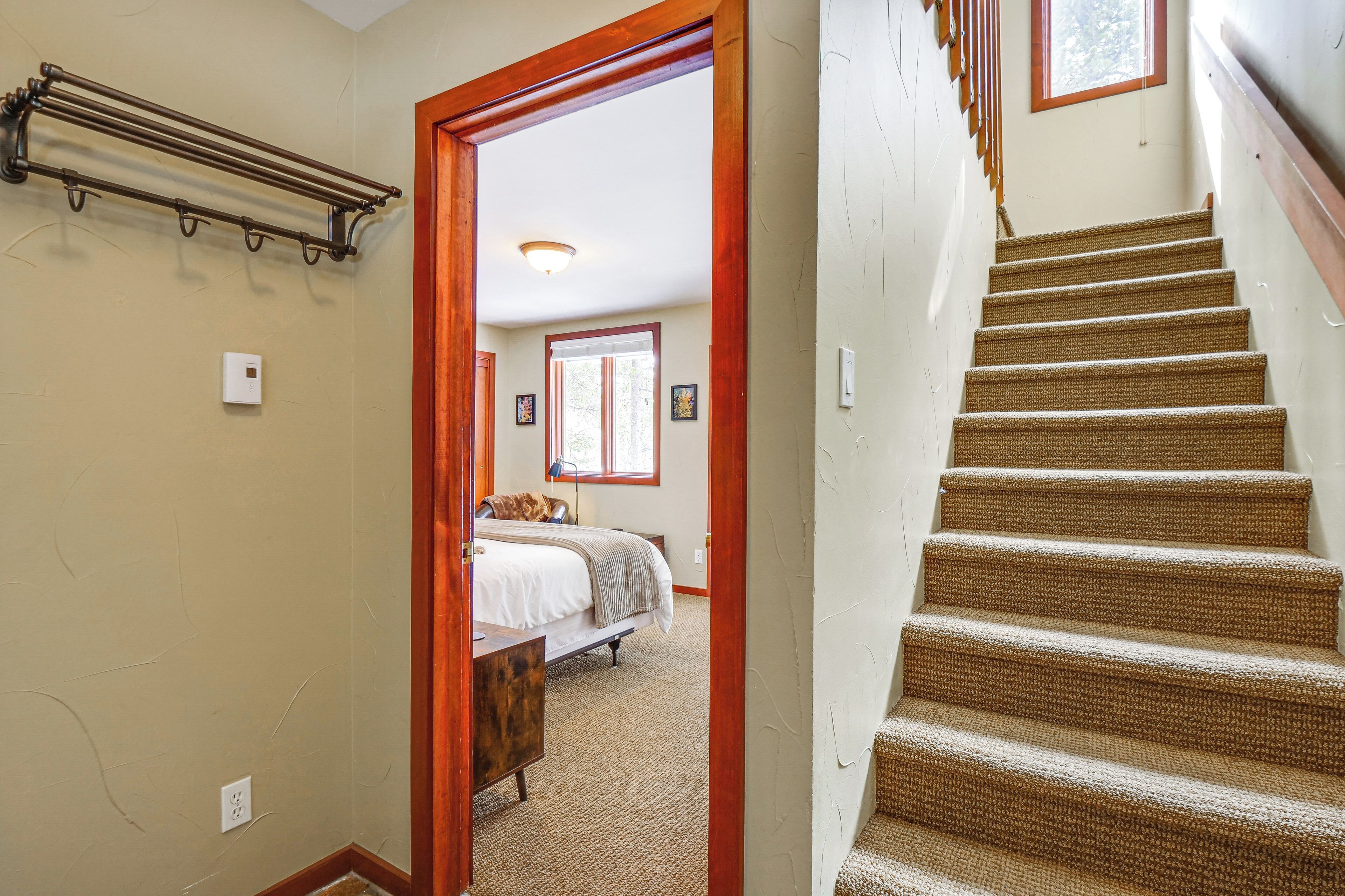 A staircase with a wooden handrail and carpeted steps leading to a bedroom with a bed and a window.